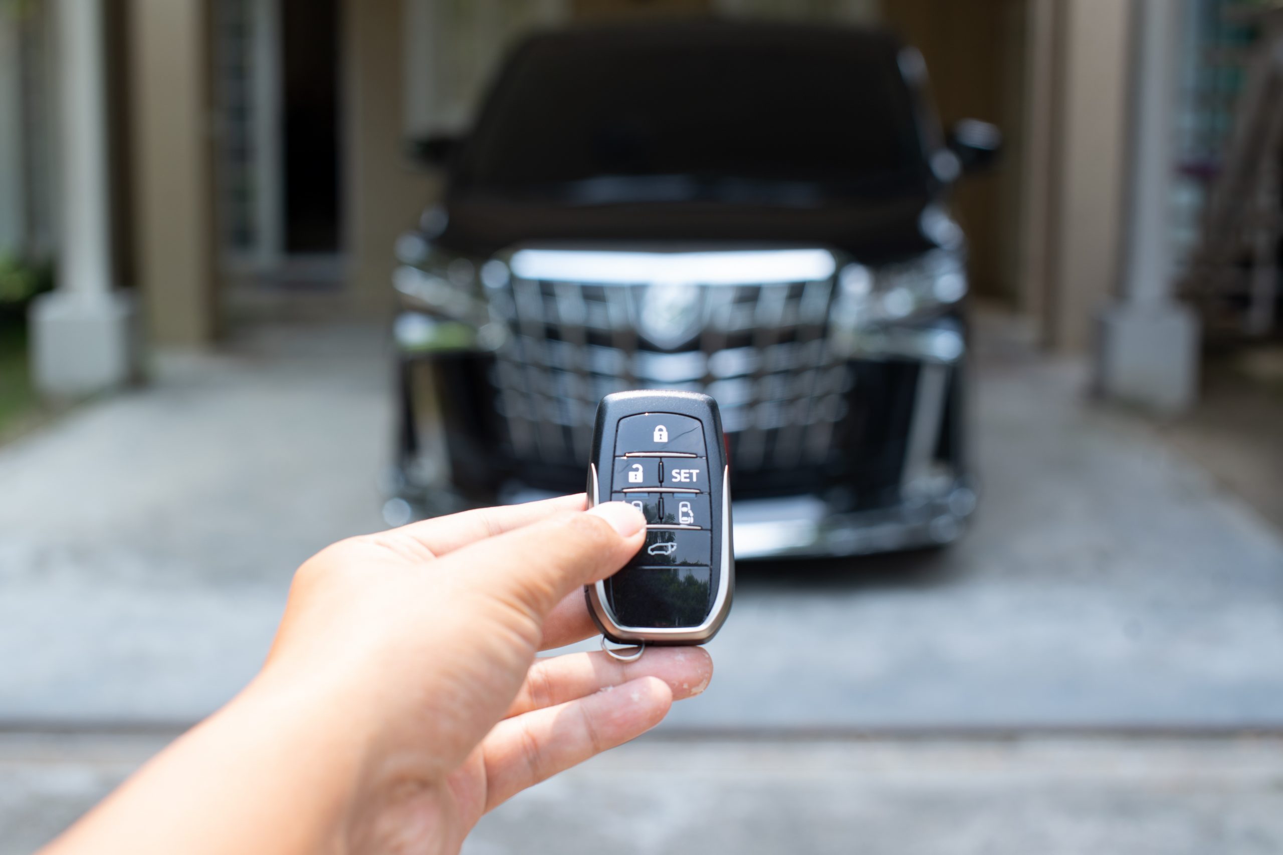 Men's hand holding car key ready to start a new car with blurred black car background.hand hold key blur car parking.